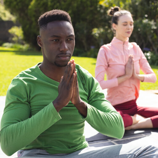 Diverse couple practicing yoga and meditating in garden. Lifestyle, togetherness, relationship, relaxation and domestic life, unaltered.